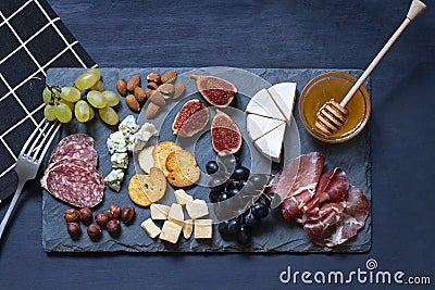 Antipasti food dark blue flat lay with nuts, honey, cured meat, salami, cheeses, grapes and figs. Stock Photo