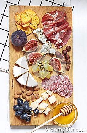 Antipasti food white flat lay with nuts, honey, cured meat, salami, cheeses, grapes and figs on the wooden board. Stock Photo