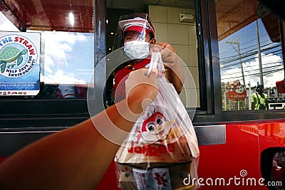 Restaurant employee with PPE serve a customer at the drive thru facility of a fast food restaurant Editorial Stock Photo