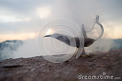 Antique artisanal Aladdin Arabian nights genie style oil lamp with soft light white smoke. Sunset mountain background Stock Photo