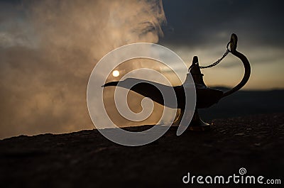 Antique artisanal Aladdin Arabian nights genie style oil lamp with soft light white smoke. Sunset mountain background Stock Photo