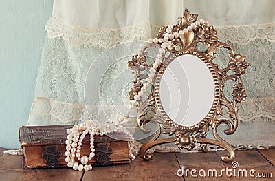 Antique blank victorian style frame and old book with vintage pearl necklace on wooden table. retro filtered image Stock Photo
