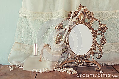 Antique blank victorian style frame, perfume bottle and white pearls on wooden table. retro filtered and toned Stock Photo