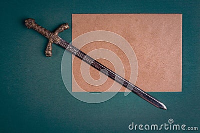 Antique knightly sword and a sheet of old paper on a green velvet background. Stock Photo