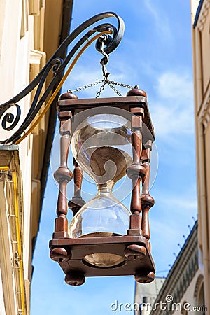 Antique large hourglass hanging in old town. Multicolored vibrant outdoors Stock Photo