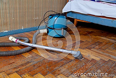 Blue vacuum cleaner stands on old parquet floor Stock Photo