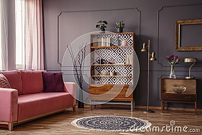 Antique wooden bookcase with decorations in an elegant gray living room interior with a comfortable powder pink sofa Stock Photo