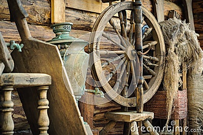 antique wooden spinning wheel with accessories and old household items against a rough wooden log wall Editorial Stock Photo