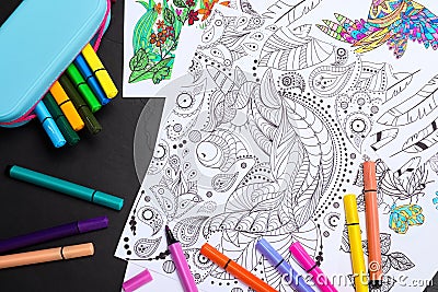 Antistress coloring pages and felt tip pens on black table, flat lay Stock Photo