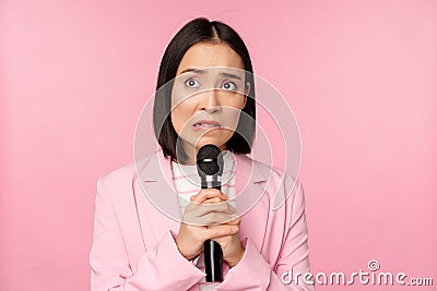 Anxious asian lady in suit, talking in public, giving speech with microphone on conference, looking scared, standing Stock Photo