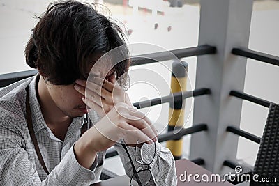 Anxious frustrated young Asian business man takes off glasses and close his eyes. he is feeling strain or tried and headache. Stock Photo