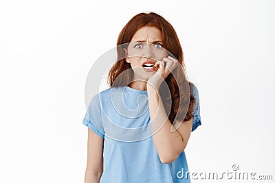 Anxious and scared redhead woman biting fingers and looking frightened, staring at camera with nervous face, fear of Stock Photo