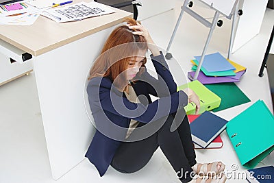Anxious upset young Asian business woman with hands on head sitting on floor at her in workplace of office. Stock Photo