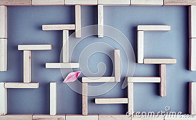 Aper boat trying to fing its way towards the exit in a maze or labyrinth made with wooden blocks. Struggle, challenge, solution or Stock Photo
