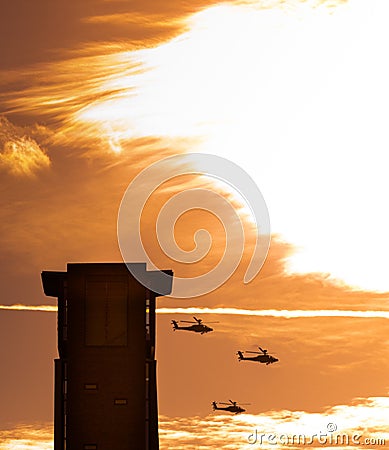 Three apache helicopters flying past a tower with clouds Stock Photo