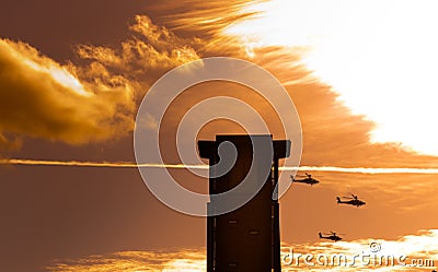 Three apache helicopters flying past a tower with clouds Stock Photo