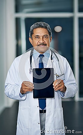 The app for doctors endorsed by a doctor. Portrait of a mature doctor holding up a digital tablet with a blank screen in Stock Photo