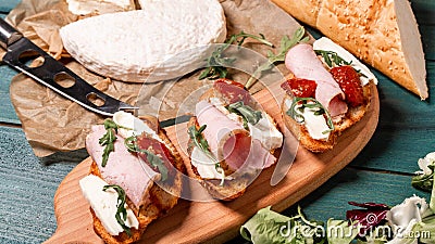 Appetizers table with italian antipasti snacks. Bruschetta with brie cheese, arugula and sun-dried tomatoes, ham. Food recipe Stock Photo