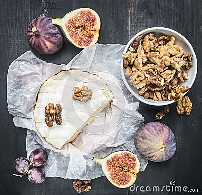 Appetizing camembert cheese, with walnuts, figs and a branch of ripe dark grapes, on a rustic wooden dark wooden background, top v Stock Photo