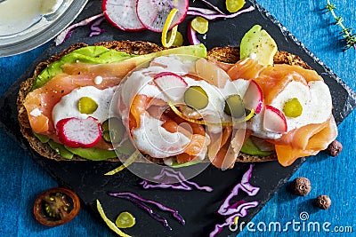 Appetizing and healthy smoked salmon with avocado, vegetables radish, lemon, red cabbage, pickle and yogurt sauce on toasted Stock Photo