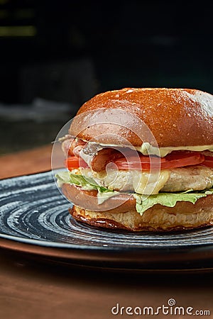 Appetizing and juicy cheeseburger with, chicken burger, tomato, caramelized onions and melted cheese in a black ceramic plate on a Stock Photo