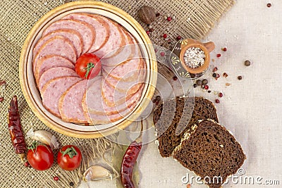 Appetizing sausage sliced on a yellow plate on a rough linen background with chilli pepers and spices close up Stock Photo