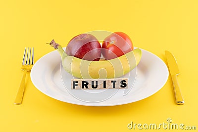 Apple, a banana and a tomato on a plate and the word 'fruits' written on wooden blocks Stock Photo