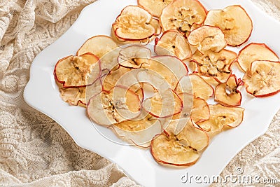 Apple chips on white figured square plate on lace fabric Stock Photo