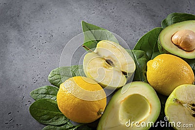 Apple halves, avocado with a stone, whole yellow lemons, ripe green spinach leaves on a gray background Stock Photo