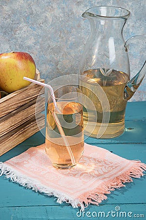 Apple juice in a glass, juice in a jug, apples in a wooden box, colored wooden background. Stock Photo