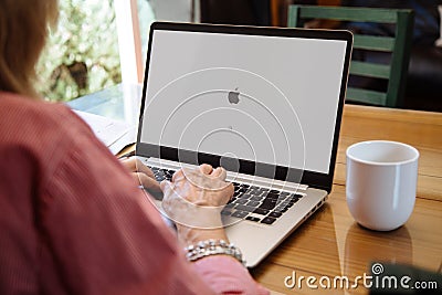 Apple logo in the screen of laptop. Mature woman sitting in front of computer with mac os Editorial Stock Photo