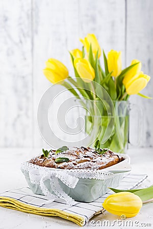 Apple pie in dishes on a white background and a bouquet of spring yellow tulips. Homemade pastries with fruit for a delicious Stock Photo