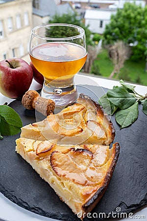 Apple products of Normandy, homemade baked apple cake, glass of cider drink and houses of Etretat village on background, Normandy Stock Photo