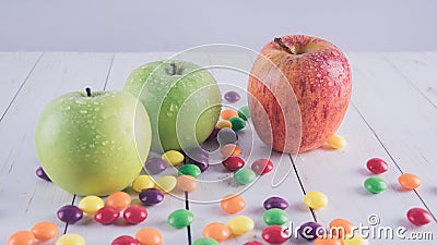 Apples and candies on a white wooden table. Harmful and healthy food on a white background. Stock Photo