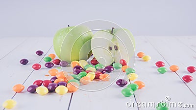 Apples and candies on a white wooden table. Harmful and healthy food on a white background. Stock Photo