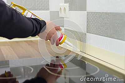Applying silicone sealant with construction syringe. Worker fills seam between the ceramic tiles on the wall and kitchen worktop Stock Photo