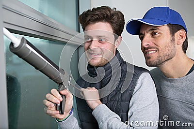 Apprentice being advised how to apply caulk to window Stock Photo