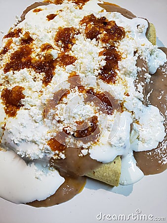 approach to a plate of enfrijoladas, traditional mexican food, tortillas bathed in bean sauce with cream, cheese and hot sauce Stock Photo