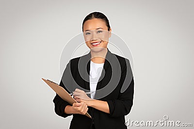 Approachable Asian businesswoman with a warm smile, holding a clipboard and pen Stock Photo