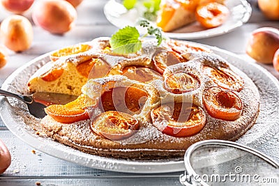 Apricot pie on a white plate, apricots, mint and powdered sugar on the kitchen table Stock Photo