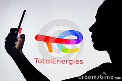 April 4, 2022, Brazil. In this photo illustration, a woman`s silhouette holds a smartphone with the TotalEnergies SE logo in the Cartoon Illustration