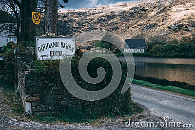 Gougane Barra Hotel sign with the Saint Finbarr`s Oratory chapel and the lake in the background. Editorial Stock Photo