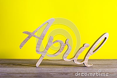 April - wooden carved word on yellow background. Spring time, 1st of april - Easter and fools day Stock Photo