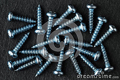 Aqua blue colored, stainless steel, pan head self-tapping screws on black stone surface. Top down, close up Stock Photo