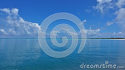 The aquamarine ocean is calm. There are picturesque cumulus clouds in the azure sky. Stock Photo