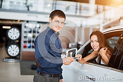 ar salesman giving car keys to young woman sitting in car in auto dealership Stock Photo