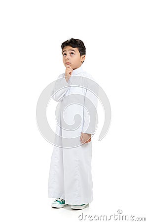 Arab boy with a confused look and his hand on chin, looking up, wearing white traditional Saudi Thobe and sneakers, raising his Stock Photo