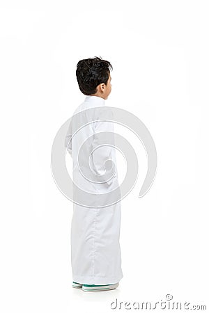 Arab boy looking at background with hand in his pockets, wearing white traditional Saudi Thobe and sneakers, raising his hands on Stock Photo