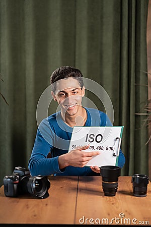 arab Guy-photographer is recording a video tutorial for photographers holding a sign with the value of ISO. Online Stock Photo