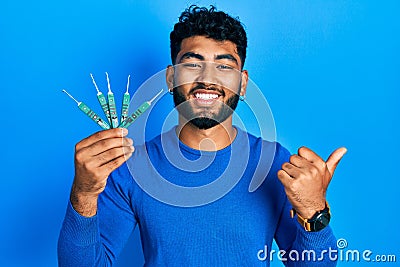 Arab man with beard holding picklock to unlock security door pointing thumb up to the side smiling happy with open mouth Stock Photo